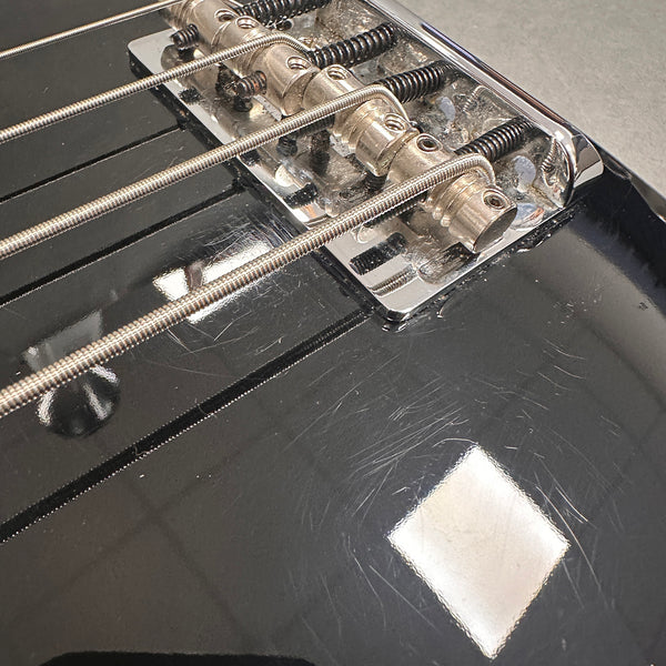 Close-up of black electric bass guitar bridge with metal saddles and strings showing surface scratches and wear