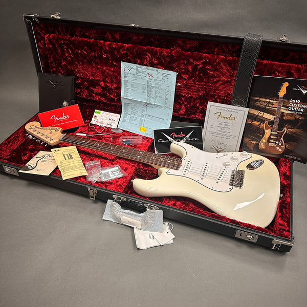 Fender electric guitar in cream finish with rosewood fretboard inside open black hardshell case with red plush interior, accompanied by Fender warranty card, certificate of authenticity, user manuals, and accessories.