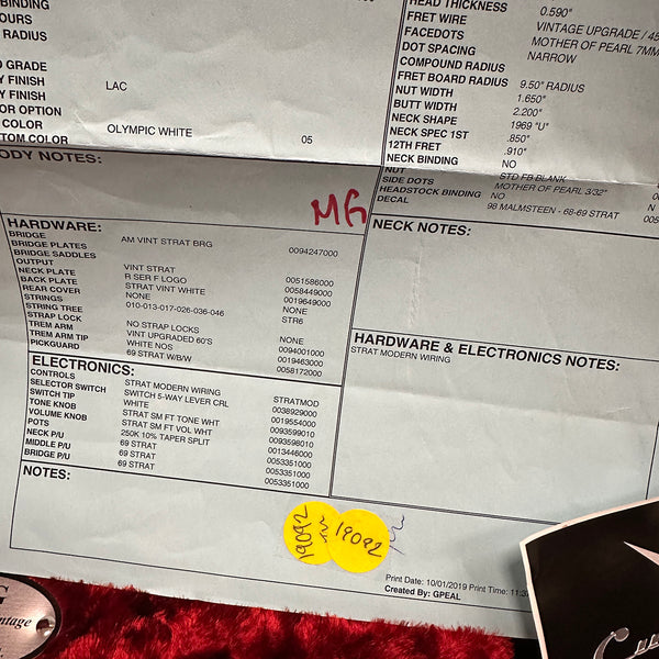 Close-up image of a vintage guitar spec sheet detailing hardware and electronics for a Strat-style guitar, including AM vintage Strat bridge, Strat modern wiring, 69 Strat pickups, and white NOS trem arm tip, on a red plush surface.