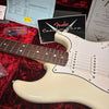 Close-up of white Fender Stratocaster electric guitar body and rosewood fretboard on red plush guitar case with Fender Custom Shop certificate and paperwork background
