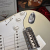Close-up of white Fender Stratocaster electric guitar body showing tone and volume control knobs, pickup, chrome bridge, and input jack in red velvet-lined case with Fender Custom Shop certificate and booklet.