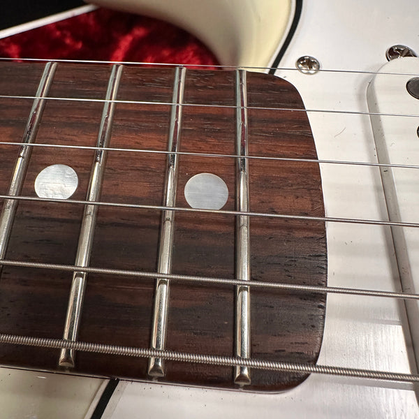 Close-up of rosewood fretboard with metal frets and dot inlays on white electric guitar body with steel strings