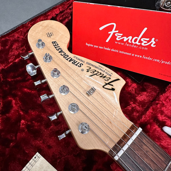 Close-up of Fender Stratocaster guitar headstock with chrome tuning pegs and maple neck in red velvet-lined case with red Fender registration card
