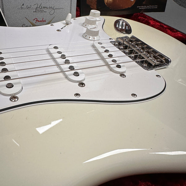 Close-up of white Fender Stratocaster electric guitar body showing pickups, tone and volume knobs, bridge, and guitar strings in red velvet-lined case.