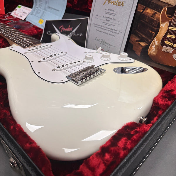 White Fender Stratocaster electric guitar in red velvet-lined black hard case with Fender Custom Shop certificate and documentation in the background