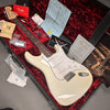 Fender electric guitar in off-white finish with rosewood fingerboard, displayed in a red plush-lined hard case with Fender warranty card, certificate of authenticity, tremolo spring instructions, and accessory tags.