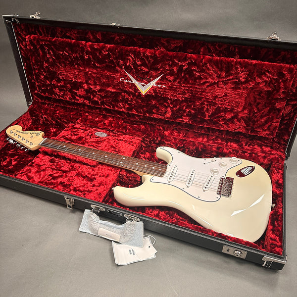 Fender Stratocaster electric guitar in off-white finish inside open black hard case with red velvet interior lining, showing guitar body, neck, and headstock with Fender logo.