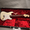 Fender Stratocaster electric guitar in vintage white finish with rosewood fretboard, displayed in an open black hard case lined with red plush fabric
