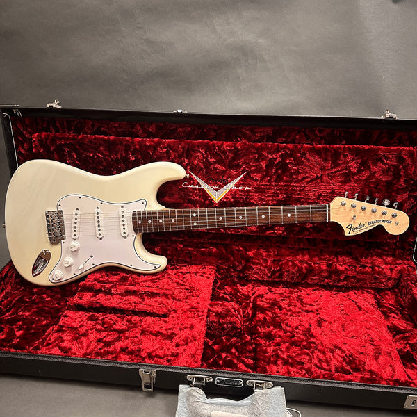 Fender Stratocaster electric guitar in vintage white finish with rosewood fretboard, displayed in an open black hard case lined with red plush fabric
