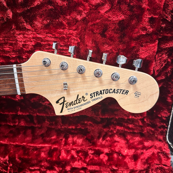 Close-up of Fender Stratocaster electric guitar headstock with tuning pegs on red plush fabric background