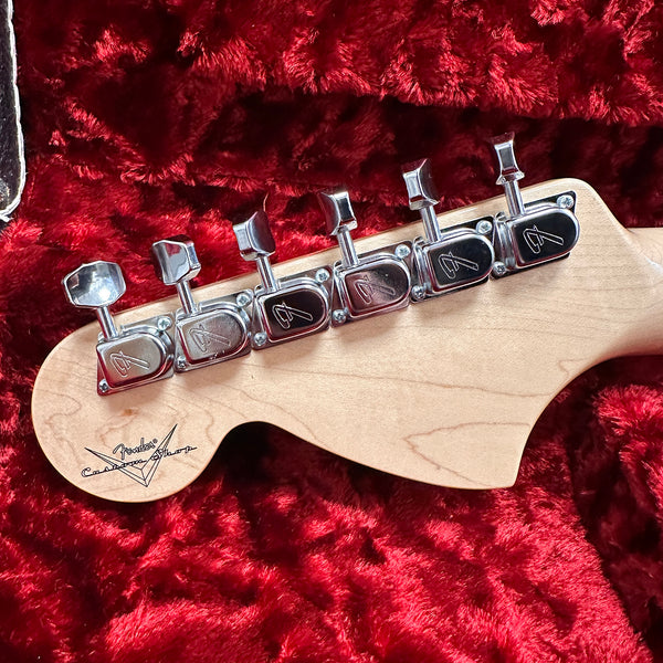 Close-up of Fender Custom Shop guitar headstock with chrome tuning pegs on red plush-lined guitar case interior