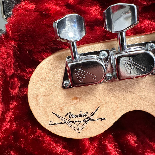Close-up of Fender Custom Shop guitar headstock with chrome tuning pegs on natural wood finish against red plush background