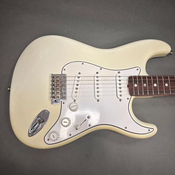 Vintage white electric guitar with three single-coil pickups and white pickguard on gray background