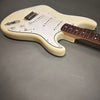 Cream electric guitar body with white pickguard, three single-coil pickups, tone and volume knobs, and rosewood fretboard on gray background.