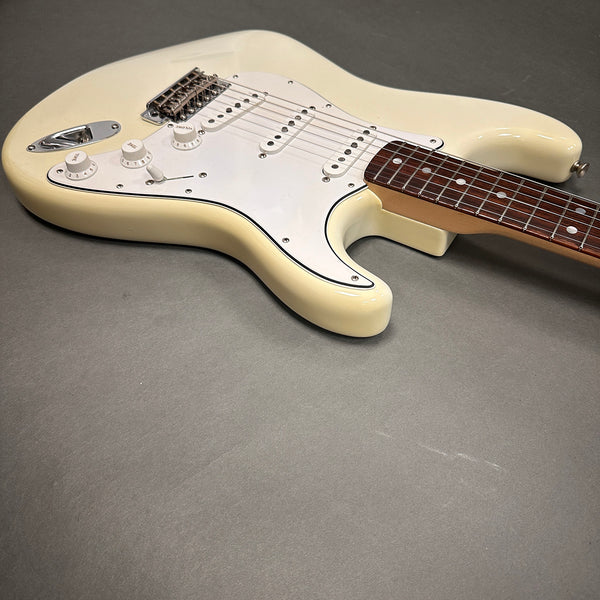 Cream electric guitar body with white pickguard, three single-coil pickups, tone and volume knobs, and rosewood fretboard on gray background.