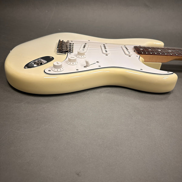 Cream-colored electric guitar body with white pickguard and three single-coil pickups on gray background