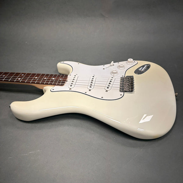 White electric Stratocaster-style guitar with three single-coil pickups, white pickguard, and rosewood fretboard on gray background.