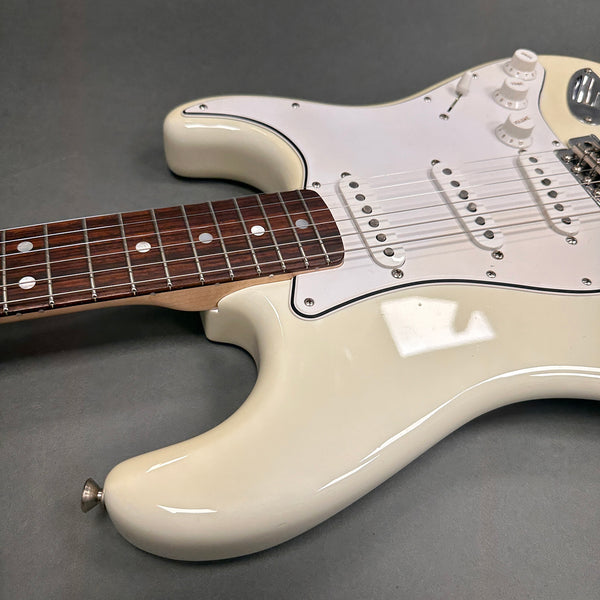Close-up of white electric guitar body and neck with rosewood fretboard and white pickguard on gray background