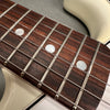 Close-up of rosewood guitar fretboard with metal frets and pearl dot inlays on white electric guitar body