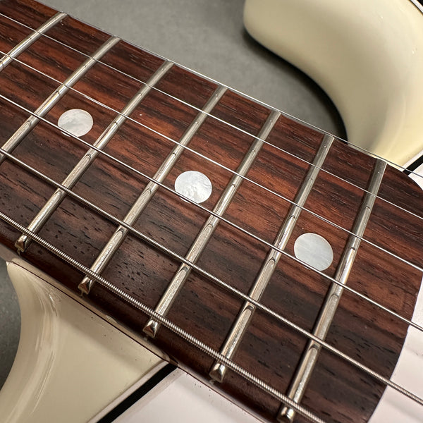 Close-up of rosewood guitar fretboard with metal frets and pearl dot inlays on white electric guitar body