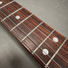 Close-up of rosewood guitar fretboard with metal frets, mother of pearl dot inlays, and steel guitar strings on gray background