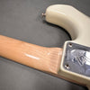 Close-up of maple guitar neck attached to cream-colored electric guitar body with chrome neck plate and serial number, on gray background