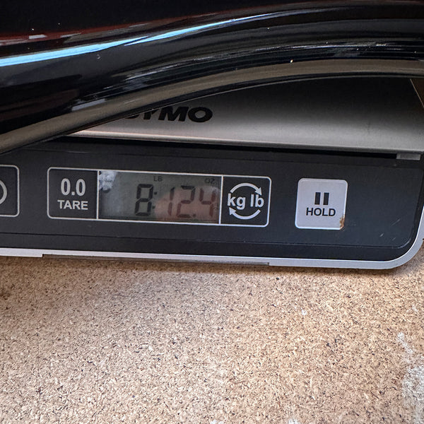 Digital scale showing guitar weight of 8 pounds 12.4 ounces on wooden surface at Coffee House Guitars.