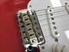 Close-up of Fender vintage-style chrome guitar bridge and white single-coil pickup on red electric guitar body