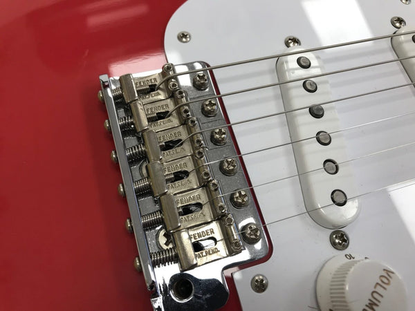 Close-up of Fender vintage-style chrome guitar bridge and white single-coil pickup on red electric guitar body