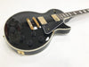 Black electric guitar with gold hardware and black control knobs on white background, solid body with cream binding and dual humbucker pickups