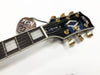 Close-up of FGN electric guitar headstock with black finish, gold tuning pegs, mother-of-pearl inlays, and a tag showing it is made by Fujigen Japan C.F.S. model