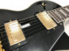 Close-up of black electric guitar body showing gold humbucker pickups, strings, and pickup selector switch with white binding around edges