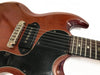 Close-up image of a vintage electric guitar body with mahogany finish, black pickguard, single-coil pickup, and rosewood fretboard showing the neck joint and strings