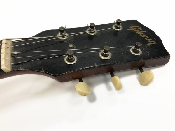 Close-up of vintage Gibson guitar headstock with six tuning pegs and black finish showing wear and patina on metal hardware and wooden edges