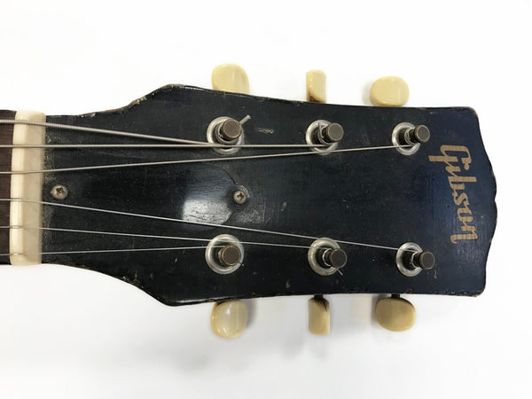 Close-up of vintage Gibson guitar headstock with six tuning pegs and worn black finish on white background