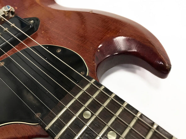 Close-up of vintage electric guitar body and neck with visible wear and aging on brown finish, black pickguard, and metal strings on rosewood fretboard