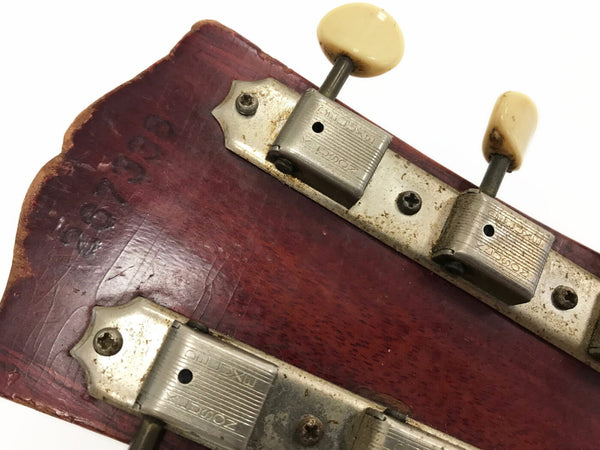 Close-up of vintage guitar headstock with aged tuning pegs and visible serial number stamped on worn wood finish