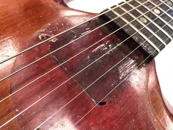 Close-up of worn vintage acoustic guitar body showing aged wood finish, soundhole, and metal strings near fretboard