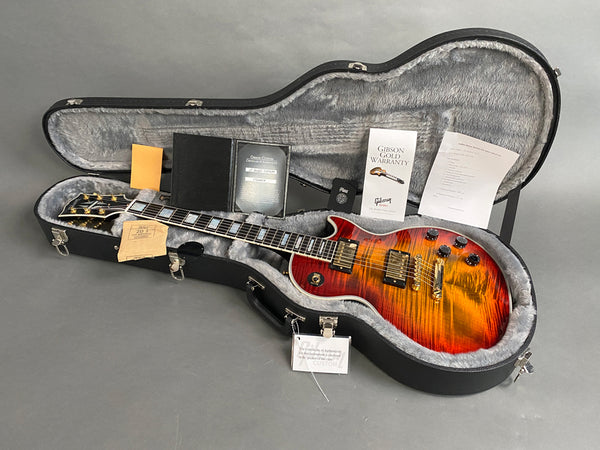 Gibson Les Paul electric guitar with flame maple top in sunburst finish, displayed inside black hard case with grey plush interior and warranty documents.