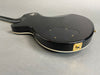 Black electric guitar body back with gold input jack and cream binding edge on gray background