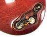 Close-up of vintage electric guitar control cavity showing potentiometers, wiring, and output jack on worn red wood finish body