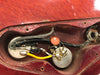Close-up view of vintage electric guitar control cavity showing potentiometers, capacitor, and wiring inside red wooden body.
