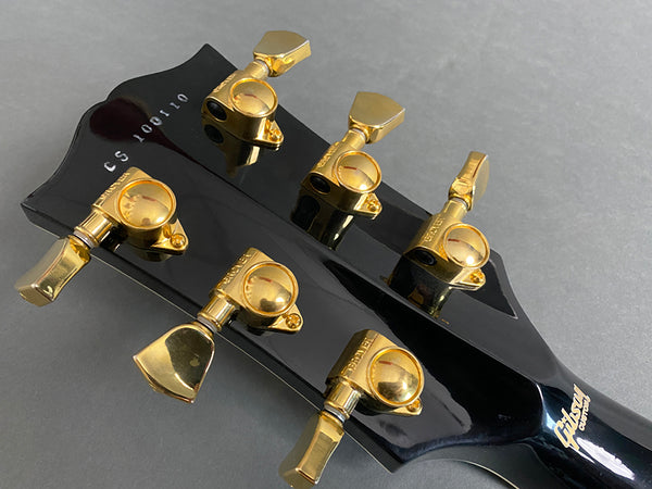 Close-up of Gibson guitar headstock with gold tuning pegs and serial number CS100110 on black finish