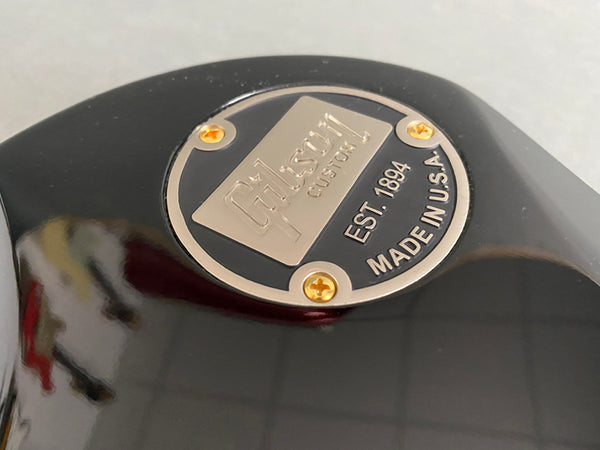 Close-up of Gibson Custom guitar metal backplate with EST. 1894 and Made in U.S.A. engraving on glossy black body