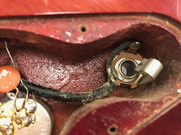 Close-up view of vintage electric guitar internal wiring showing potentiometer and input jack cavity with cloth-covered wire and capacitor component