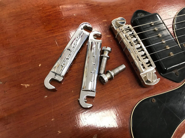 Close-up of a vintage electric guitar's bridge with two chrome tailpiece parts and mounting screws placed on the wooden body near the black pickup and pickguard.