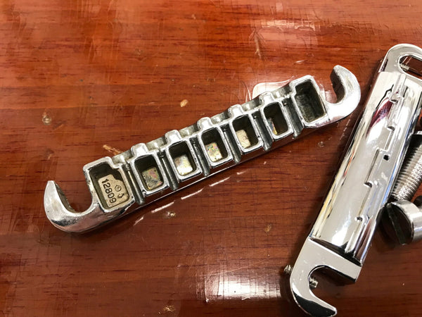 Vintage chrome Tune-o-Matic guitar bridge and tailpiece on wooden surface with serial number 12809 visible