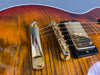 Close-up of gold bridge and humbucker pickup on sunburst electric guitar with flame maple top
