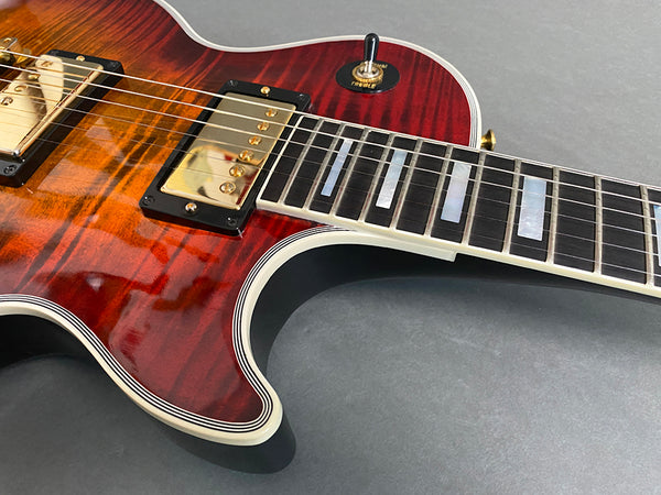 Close-up of a sunburst electric guitar body with gold humbucker pickups and cream binding on the neck and body edges on a gray background