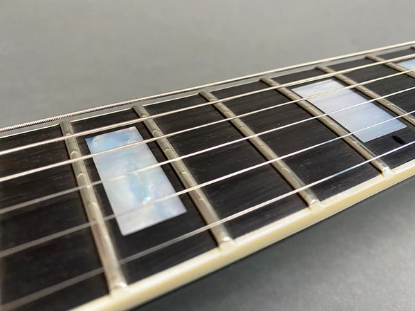 Close-up of guitar fretboard with rectangular mother of pearl inlays and metal frets on dark wood fingerboard